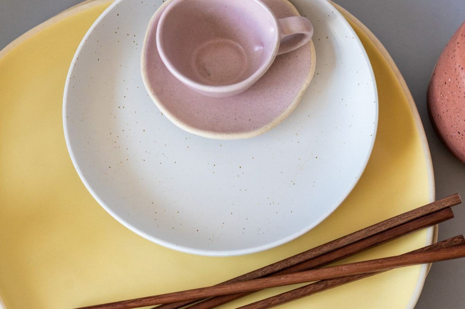 Assiettes empilées, une tasse rose et des baguettes en bois