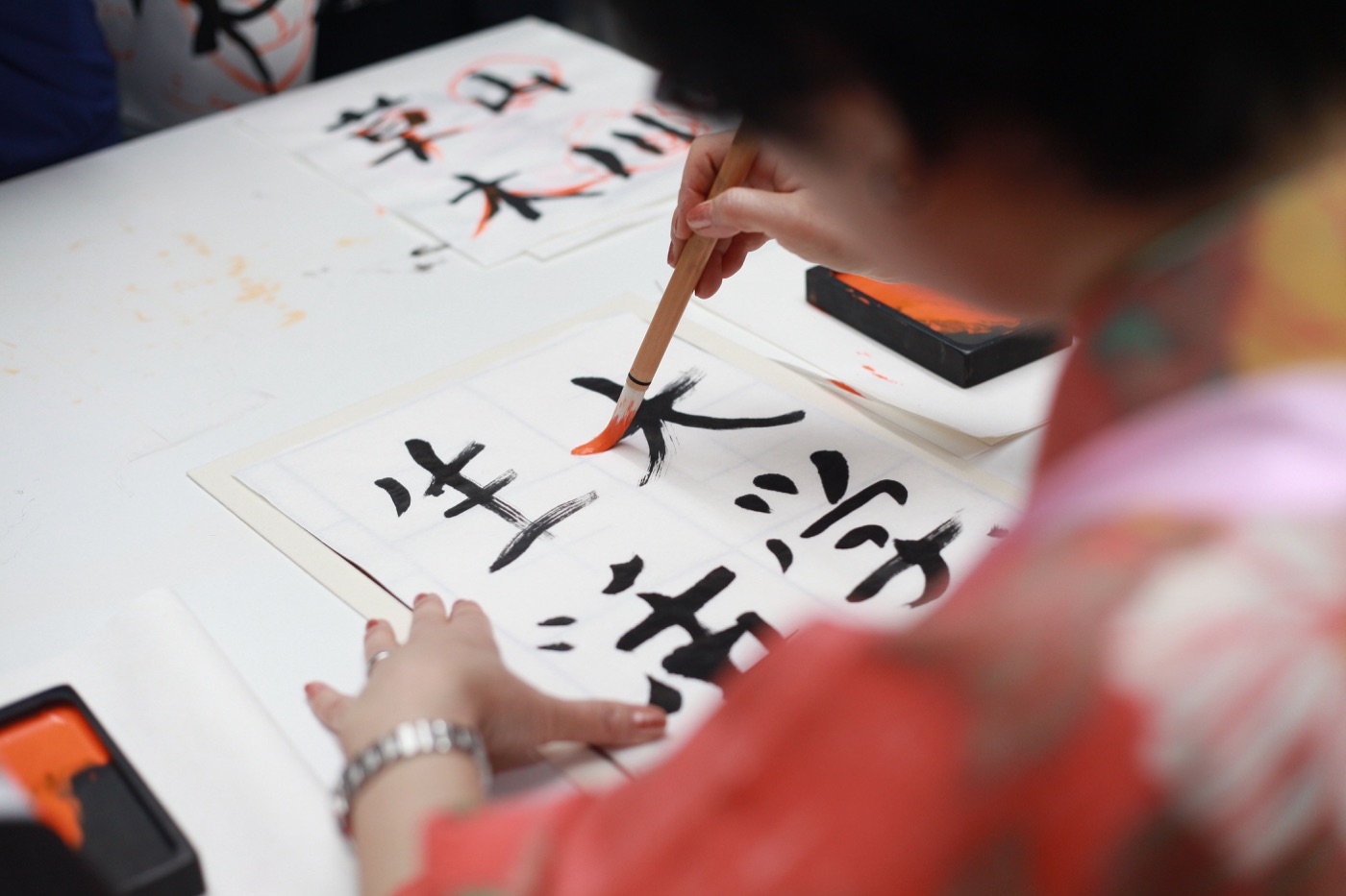 Personne en train d'écrire des kanji au pinceau sur une feuille quadrillée