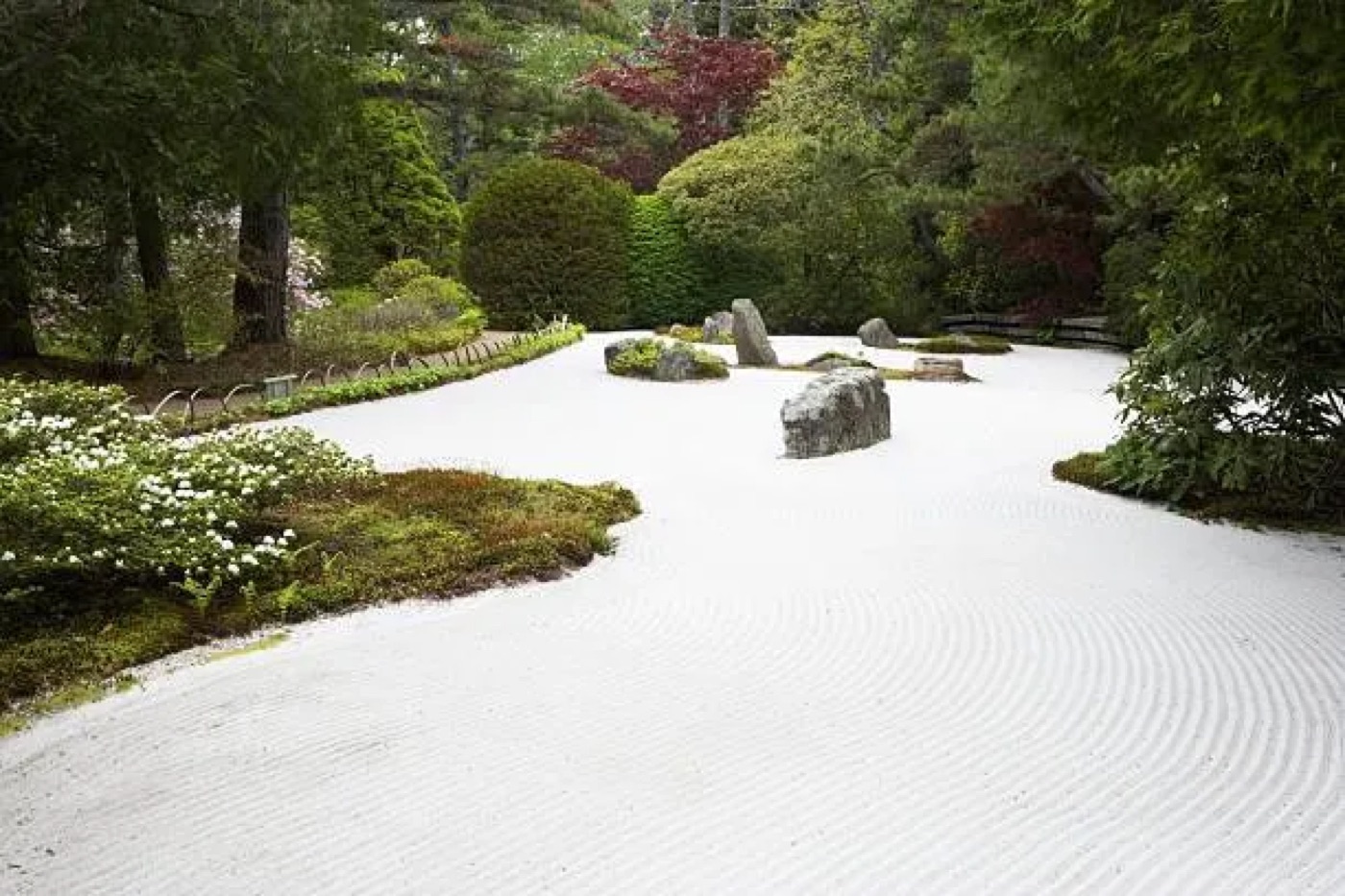 Jardin de gravier ratissé bordé d'arbres, dont quelques feuillages rouges en arrière-plan
