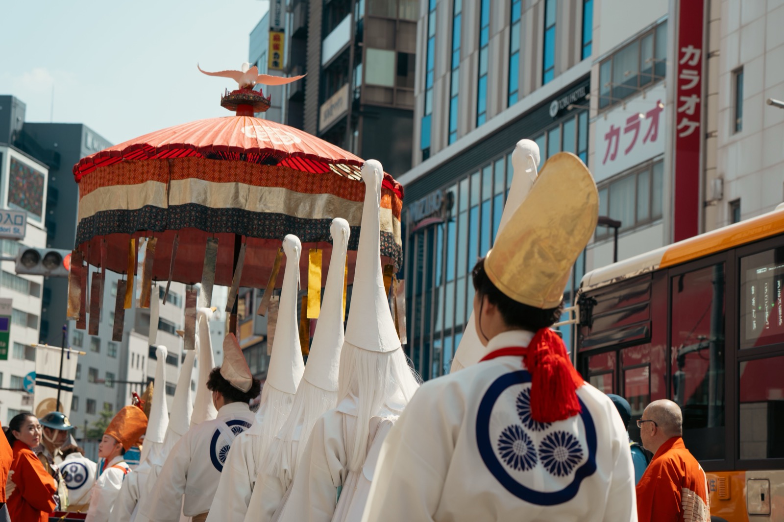 Procession de matsuri dans une rue japonaise, porteurs en habits traditionnels blancs sous une ombrelle rituelle