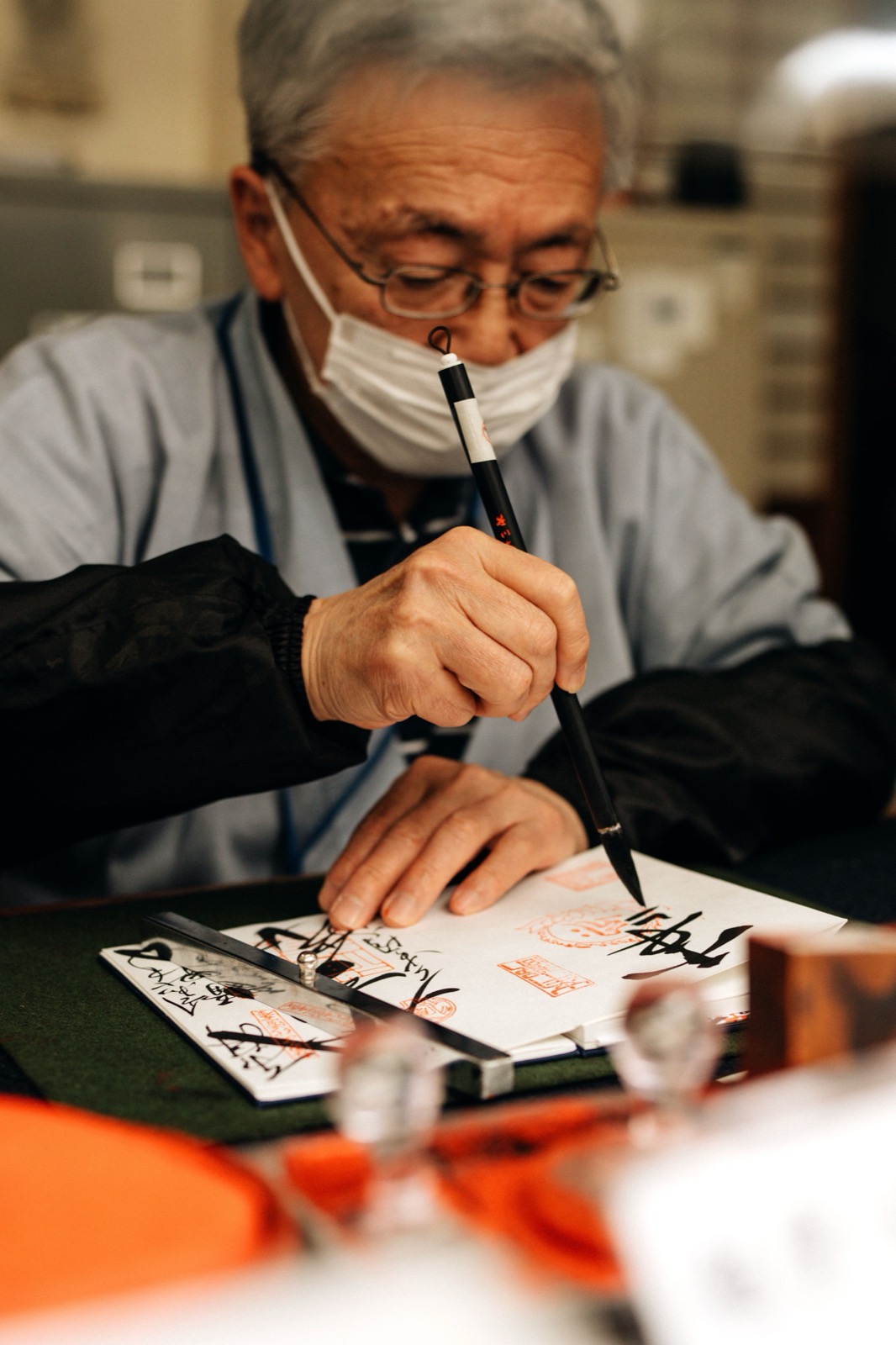 Un homme âgé calligraphie un kanji au pinceau dans un carnet goshuinchō