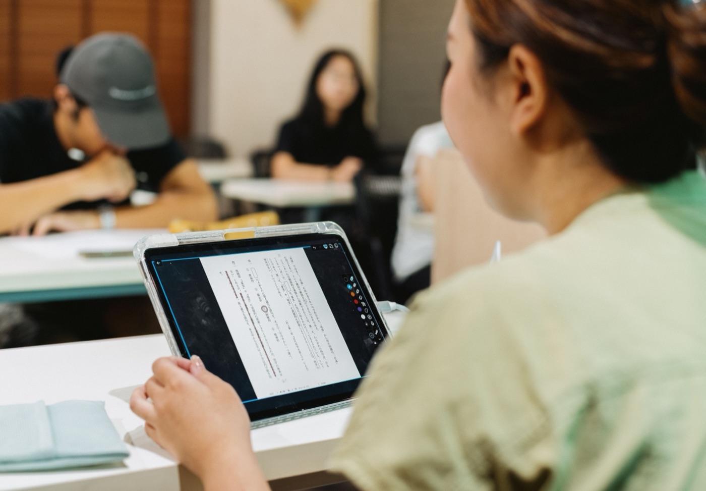 Élève japonaise révisant sur tablette en classe, texte en japonais visible à l'écran