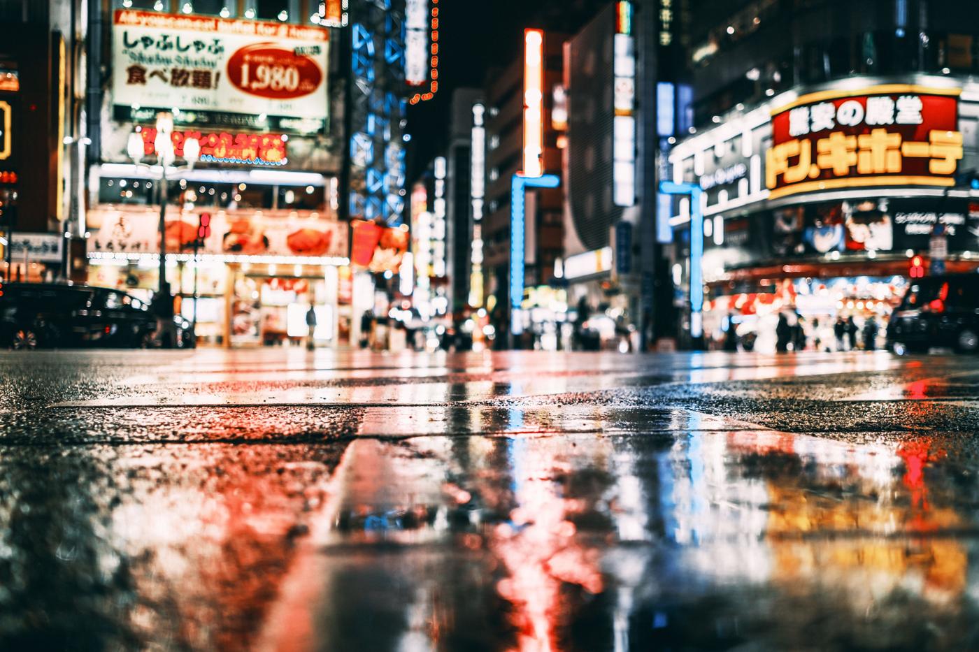 Une rue de Tokyo la nuit, les enseignes lumineuses se reflètent sur le sol mouillé