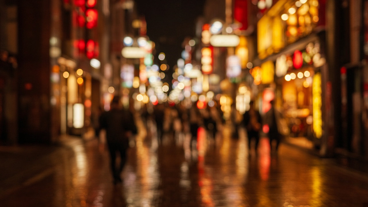 Rue commerçante japonaise la nuit, enseignes lumineuses floues et chaussée mouillée