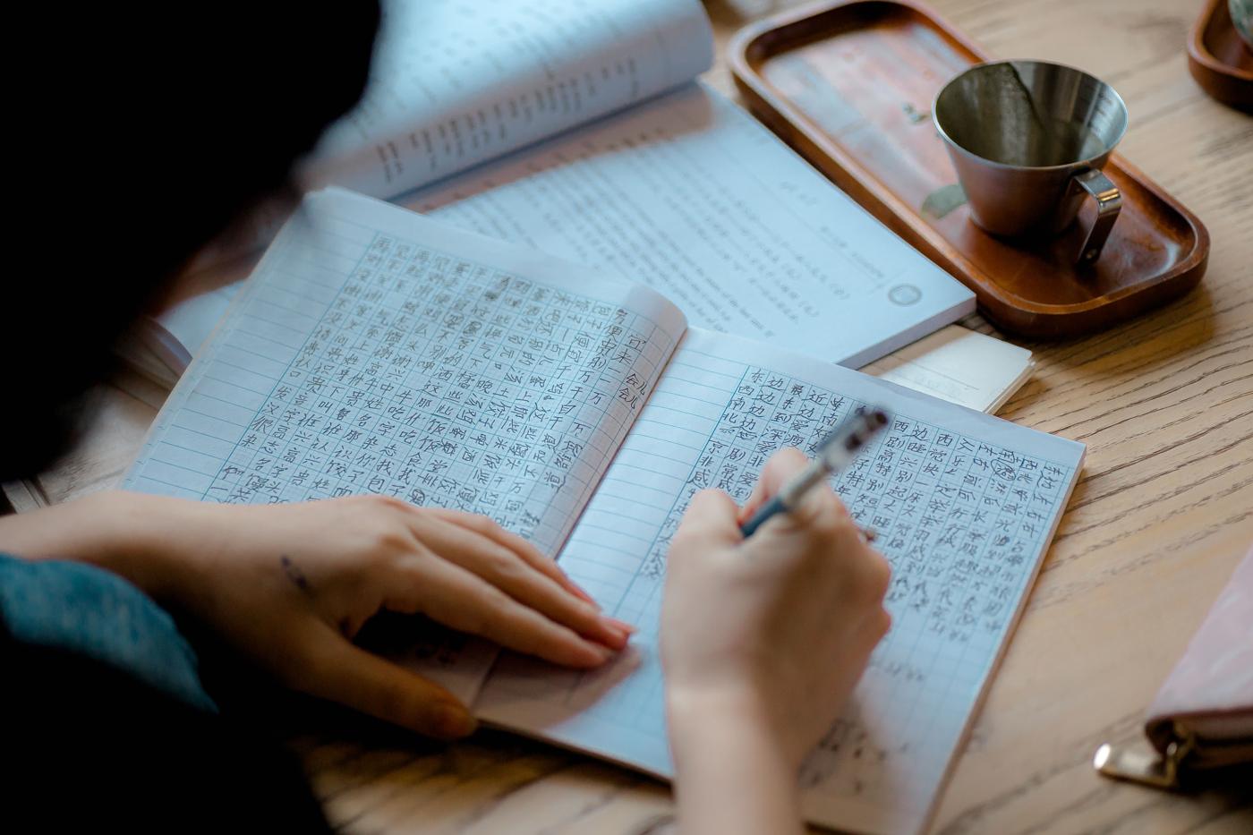 Une personne recopie du japonais dans un cahier, à côté d'une tasse de thé